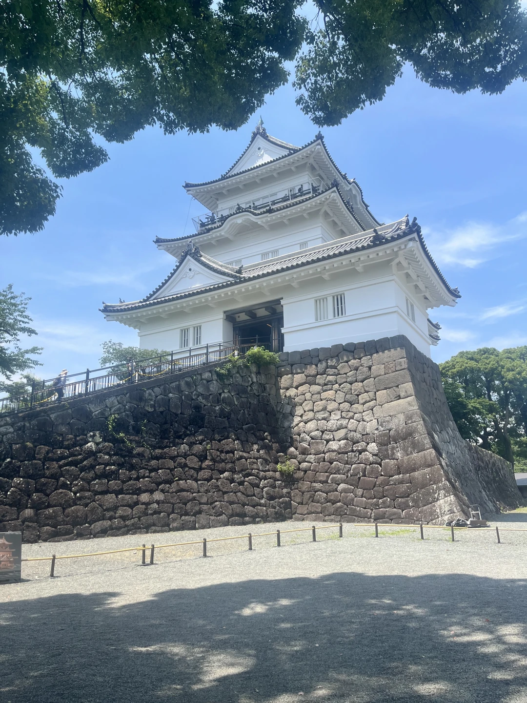 青空と木々を背景に、石垣の上にそびえる白い城の天守